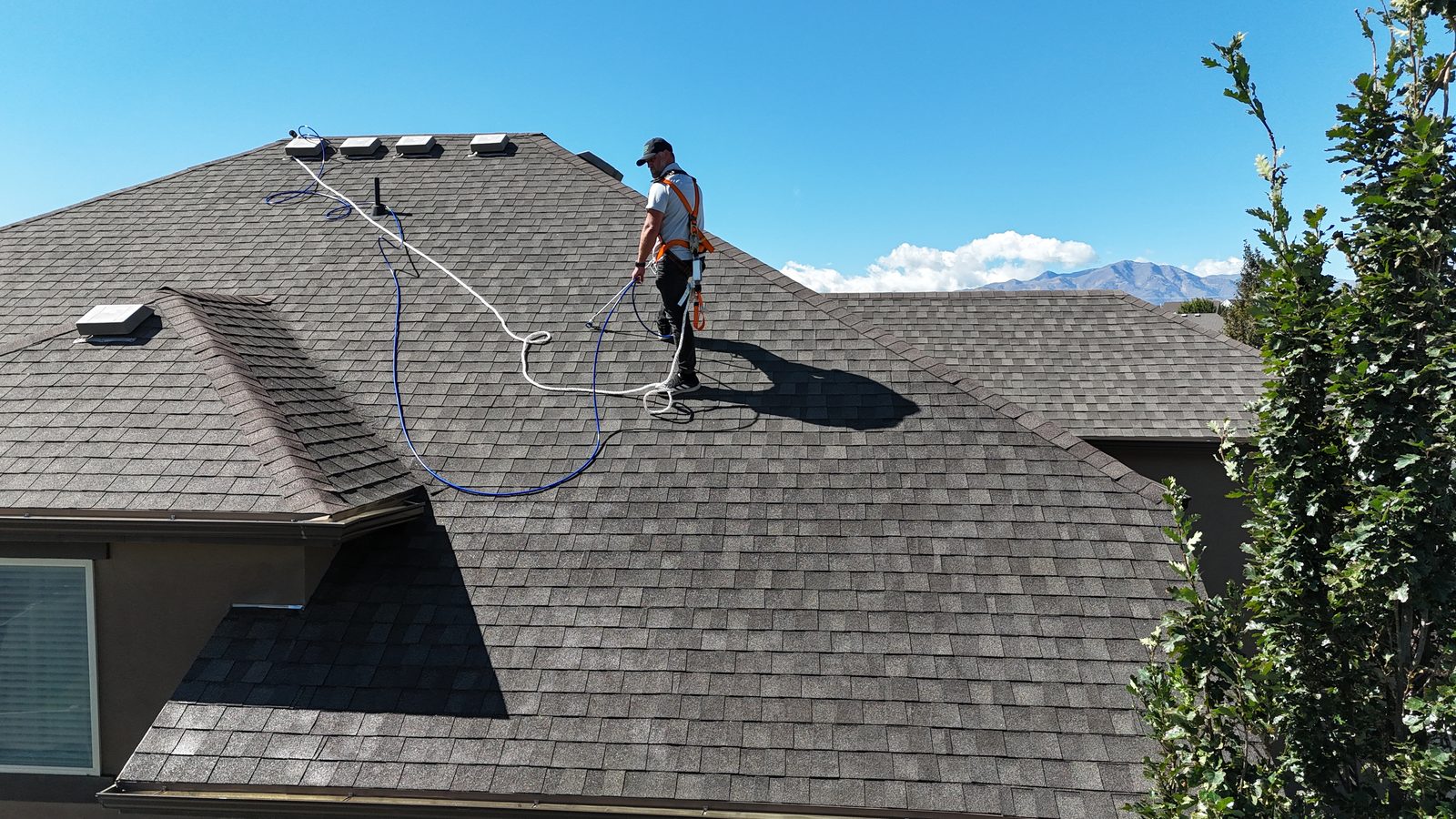 An applicator in a harness on the roof mid-job, with the treated section darker than the untreated section.