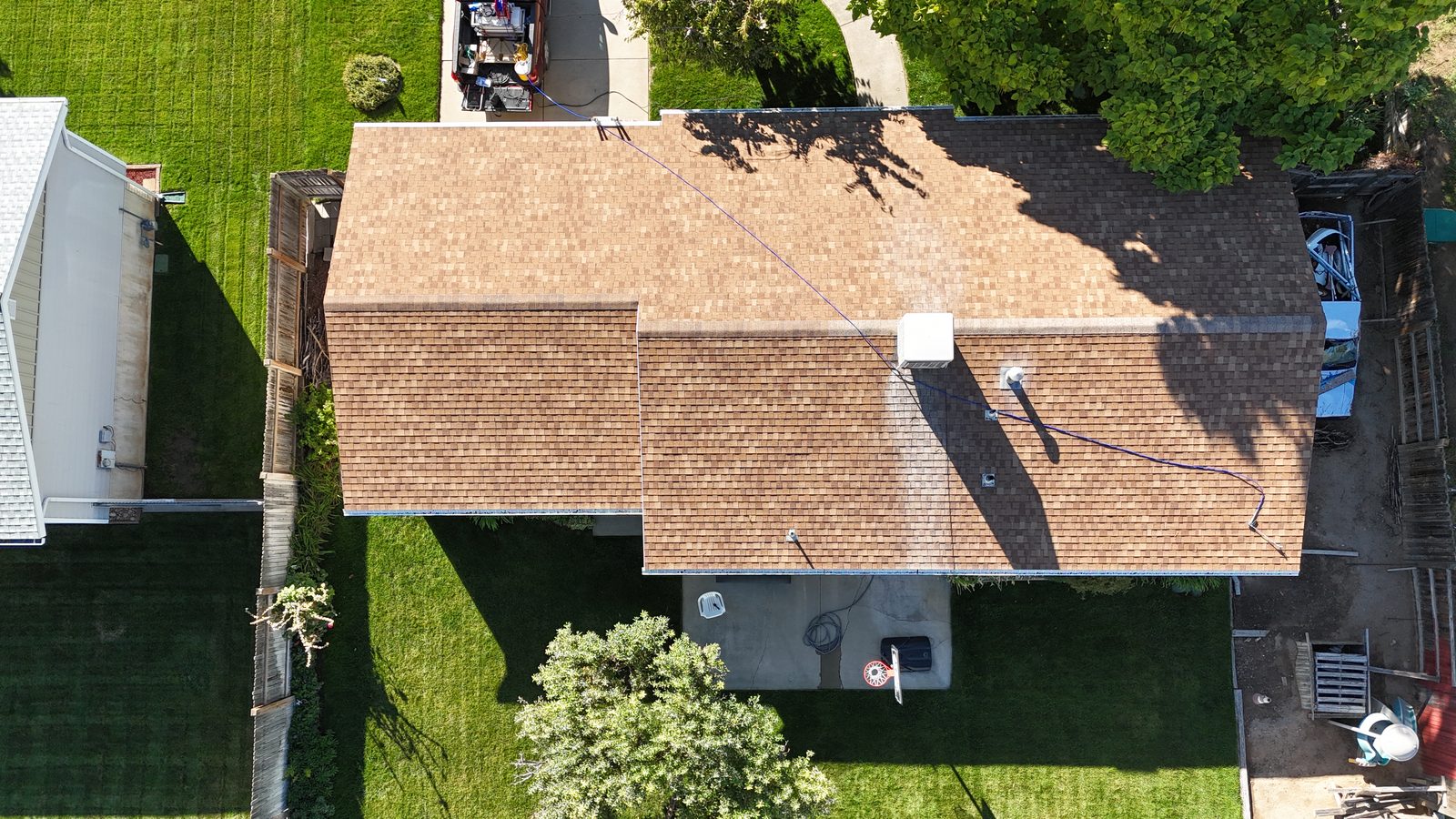 Overhead view of a single-storey home's tan asphalt shingle roof with a spray hose across it, partway through treatment.